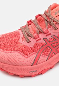 Gros plan sur une chaussure de course ASICS corail rose avec des lacets à motifs et une semelle texturée portant l'inscription FF Blast pour l'amorti.