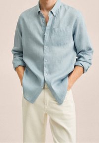 Jasnoniebieska koszula zapinana na guziki, wykonana z teksturowanej tkaniny, z kieszenią na piersi, podwiniętymi rękawami i luźnym krojem, zestawiona z kremowymi spodniami.
