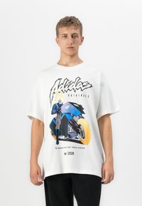 Ung mann iført en hvit t-skjorte med Ghost Rider på en motorsykkel med brennende hjul og fet "Adidas Originals" tekst.