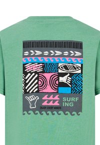 Camiseta de algodón verde con un gráfico de múltiples patrones en negro, rosa, azul y gris, que incluye texto sobre surf y símbolos de manos.