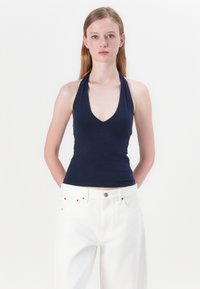 Mornarica halter top s dubokim V-izrezom, izrađen od mekane, rastezljive tkanine, u kombinaciji s bijelim trapericama visokog struka.