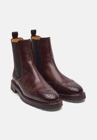 Stivali Chelsea in pelle marrone scuro con finitura testurizzata, dotati di pannelli elastici e perforazioni decorative sulla punta, suola robusta.