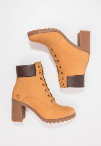 Bottines à lacets couleur fauve avec un revers en cuir marron, un talon épais marron et une semelle en caoutchouc texturée avec des œillets dorés pour les lacets.