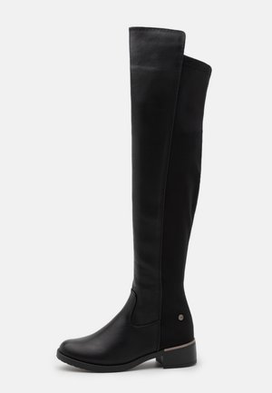 Bottes noires au-dessus du genou en cuir, avec une finition lisse, un léger talon et un bout rond. Comprend un détail de quincaillerie décoratif.