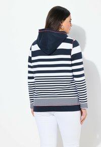 Pull-over rayé avec une capuche marine et des accents blancs, présentant des rayures horizontales en marine et blanc, avec une bordure rouge le long de l'ourlet.