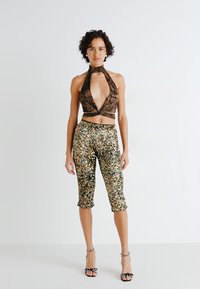 Haut crop en bronze avec un décolleté en V profond, accompagné de pantalon à sequins longs jusqu'aux genoux en or et argent. Talons avec des accents noirs et blancs.