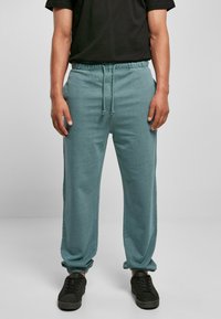 Lys teal joggebukser laget av mykt stoff, med elastisk midjebånd og snøring, samt elastiske mansjetter ved anklene.