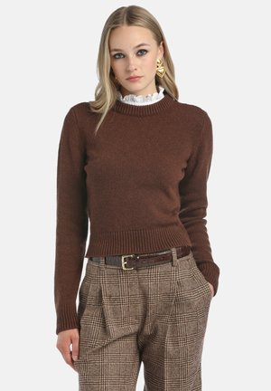 Bruine gebreide trui met geribde kraag en manchetten, gecombineerd met bruin en beige geruite broek en een donkere riem, wat zorgt voor een textuurrijke uitstraling.