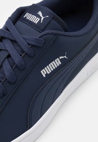 Baskets Puma bleu marine avec bande latérale texturée, logos blancs Puma sur la languette et sur le côté, lacets bleu marine et semelle blanche.