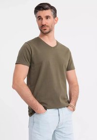 Olivově zelené bavlněné tričko s v-neck výstřihem a krátkým rukávem, volný střih, minimalizované švy, kombinované se světle modrými džíny.