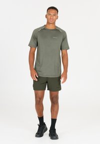 Grön träningsskjorta med korta ärmar och reflexdetaljer, matchad med mörkgröna shorts. Modellen bär svarta sneakers och strumpor.