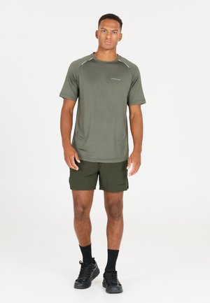 T-shirt de sport vert à manches courtes avec des accents réfléchissants, associé à un short vert foncé. Le modèle porte des baskets noires et des chaussettes.