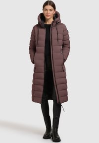 Lang dunjakke i mørk mauve med hætte, lynlås foran, quiltet struktur og sidelommer, parret med sorte leggings og støvler.