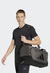 Bolsa de viaje negra y gris con múltiples bolsillos con cremallera, tela texturizada y logo impreso. Correa de hombro desmontable.