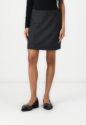 Jupe grise à rayures côtes, en tissu doux, mi-longue, avec une silhouette ajustée. Associée à des chaussures en cuir noires avec des accents décoratifs.