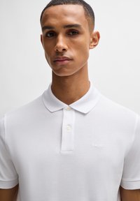 Hvit polo skjorte laget av teksturert stoff, med klassisk krage, to knapper foran og liten brodert "BOSS"-logo på brystet.