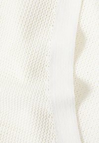 Detailní pohled na krémově bílou pleteninu s texturovaným diamantovým vzorem a pevným svislým pruhem na oděvu.