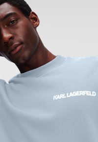 Svijetloplava dukserica s okruglim izrezom i bijelim logom "KARL LAGERFELD" na prsima. Glatka tekstura, ležeran stil.