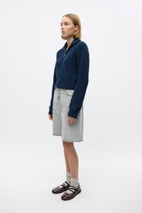 Suéter de punto azul marino con cremallera, pantalones cortos de mezclilla gris claro, zapatos negros y burdeos con correas, y calcetines grises doblados. Atuendo simple y casual.