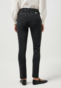 Jeans negros ajustados de cintura media, con dos bolsillos traseros que presentan un patrón de puntada en zigzag y un sutil logo en el bolsillo.