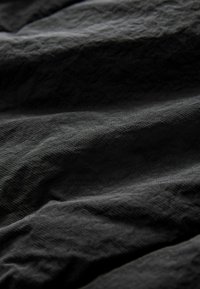 Tissu noir texturé avec des plis prononcés et un subtil éclat, mettant en valeur une structure tissée légère et une surface lisse.