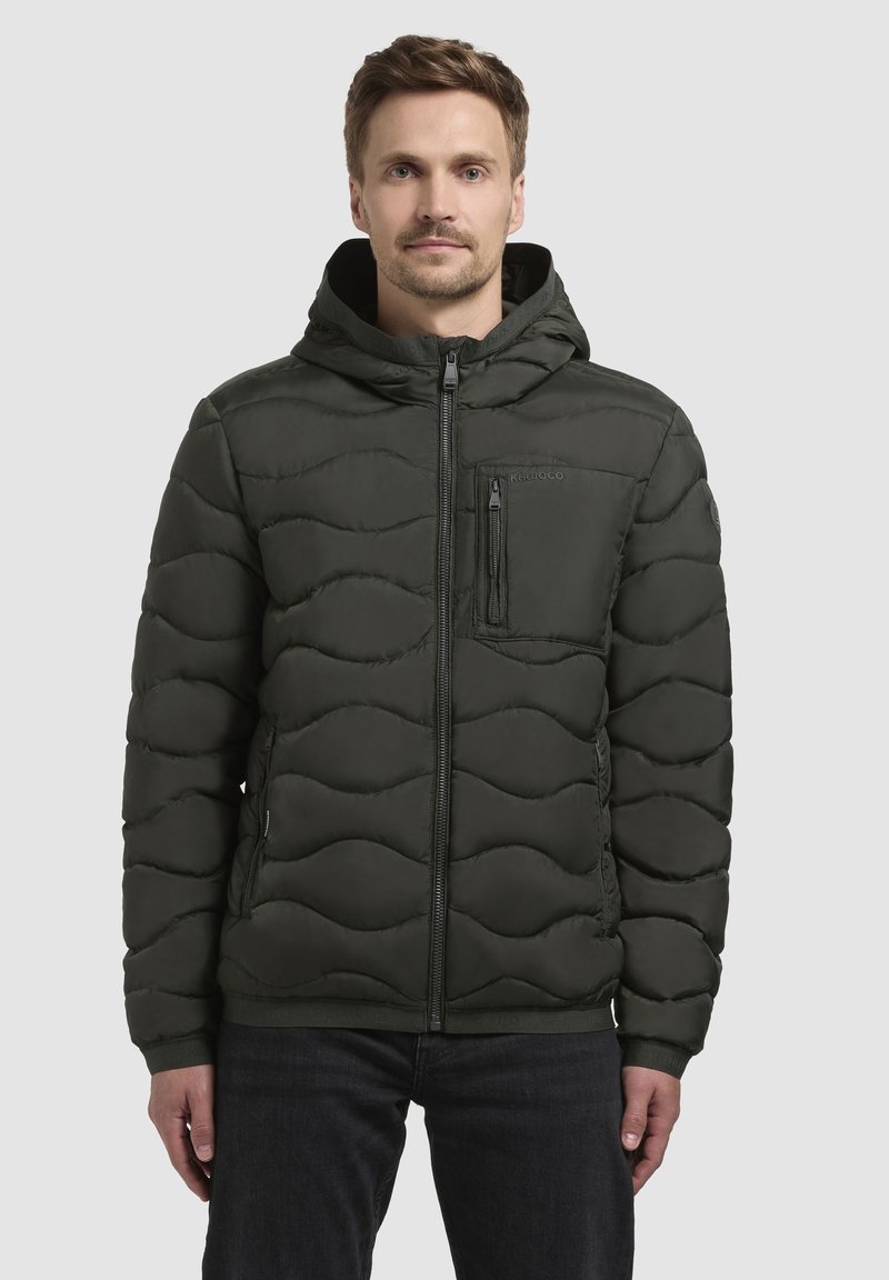 Dunkelgrüne Steppjacke mit Kapuze, gestepptem Wellenmuster, Vorderreißverschluss und Reißverschluss-Brusttasche. Glatte, leicht glänzende Textur.