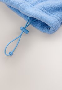 Tissu polaire bleu clair avec un cordon de serrage réglable et une fermeture à pression en plastique sur une surface claire.