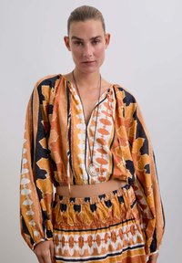 Top corto multicolor y falda a juego con patrones audaces en naranja, negro y blanco. Tejido ligero con detalles fruncidos.