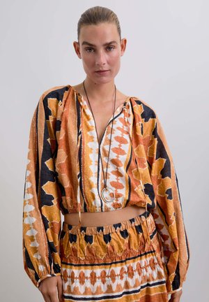 Top corto multicolor y falda a juego con patrones audaces en naranja, negro y blanco. Tejido ligero con detalles fruncidos.