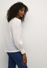 Vit blus med texturerade prickar, puffärmar och samlade manschetter. Kombinerad med blå denimjeans. Enkelt, elegant design.