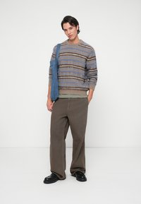 Knit sweater in beige with blue and brown stripes, paired with loose brown pants. A blue denim tote bag is draped over one shoulder.
