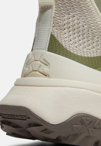 Gros plan sur la partie supérieure en maille texturée beige, la languette de traction et la semelle épaisse beige avec une semelle extérieure TimberGrip foncée et robuste du talon d'une basket.