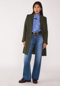 Cappotto di lana verde oliva, blusa a righe blu con volant, jeans chiari a zampa d'elefante e scarpe marroni con lacci. Design semplice con vestibilità sartoriale.