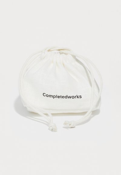 Balta kokvilnas zīmuļmaiss ar teksturētu virsmu, ar melnu "Completedworks" logo, kas izdrukāts vienā pusē.