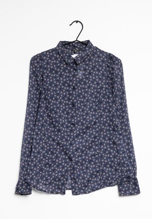 Chemise bleu marine à boutons avec motif géométrique blanc et rose, manches longues et col pointu sur cintre noir sur fond blanc.