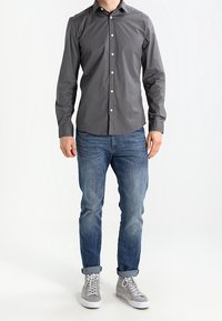 Grå langærmet skjorte med knaplukning foran, kombineret med blå jeans og grå højtop-sneakers. Har en ren, glat tekstur.