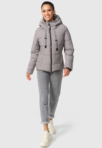 Grijze pufferjack met een capuchon, rits aan de voorkant en trekkoorden; gecombineerd met lichtgrijze broeken en witte sneakers. Soepele textuur en gewatteerd patroon.