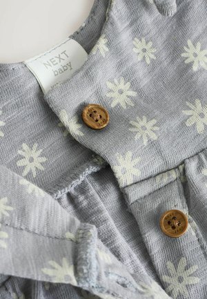 Indumento in tessuto grigio con leggeri motivi floreali, dotato di bottoni in legno e un'etichetta che legge "NEXT baby." Texture morbida e design casual.