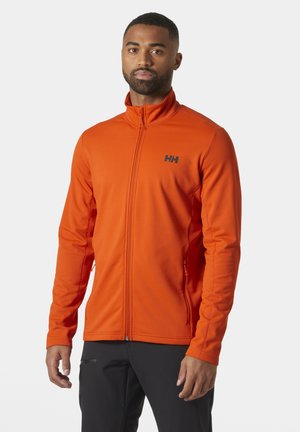 Chaqueta naranja con cremallera hecha de un tejido texturizado y ligero. Presenta un cuello alto y un logo negro en el lado izquierdo del pecho. Tiene bolsillos.