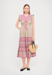 Grønn blomstermønstret kjole med volanger og rosa accenter. Den har en lagdelt skjørt og frynse-knytte. Kombinert med en flettet håndveske.