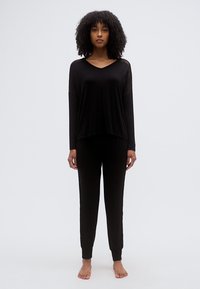 Μαύρο σετ ρούχων για χαλάρωση με φαρδιά μπλούζα μακριάς μανίκας και V-λαιμόκοψη, και ταιριαστό στενό παντελόνι, φτιαγμένα από μαλακό ύφασμα.