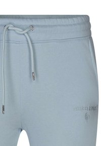 Pantalon de survêtement bleu clair en tissu doux, avec taille à cordon de serrage, œillets argentés et détail de logo embossé sur le côté.