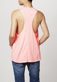 Ärmfritt korallfärgat linne med rundad nederkant och öppen ryggdesign. Tillverkat av lätt tyg med en mjuk textur.