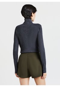 Maglione a collo alto a coste di colore grigio scuro, design attillato, maniche lunghe, abbinato a pantaloni corti verdi oliva, texture liscia, dettagli minimi.