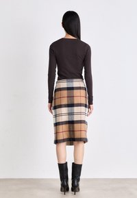 Haut marron à manches longues associé à une jupe de longueur genou avec un motif vichy beige, marine et rouge. Porté avec des bottes à talons noires.