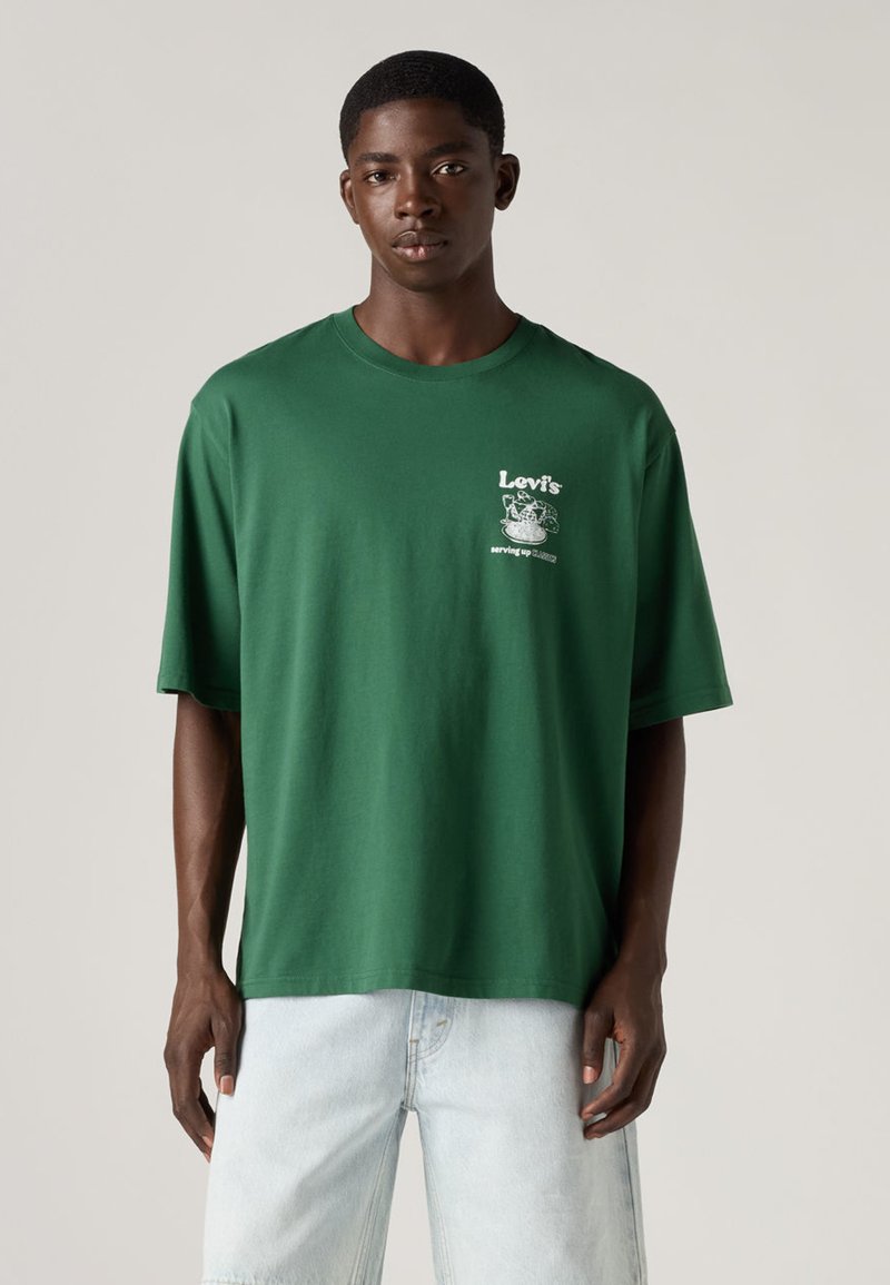 Grünes Baumwoll-T-Shirt mit lockerem Schnitt, kurzen Ärmeln und rundem Ausschnitt. Auf der Brust befindet sich ein weißer, grafischer Aufdruck.