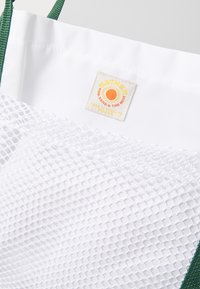 Sac fourre-tout blanc avec un fond en maille et des bretelles vertes. Présente une étiquette de marque affichant un logo de soleil avec le texte "BATHER". Construction en tissu durable.
