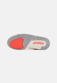 Světle šedá podrážka s červeným kulatým vzorem a texturovanými akcenty; obsahuje logo "JORDAN" v červené; hladká béžová mezipodešev se šedými detaily.