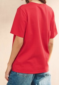 Red cotton t-shirt with short sleeves and a round neckline, featuring a relaxed fit and a smooth texture, paired with blue denim jeans.