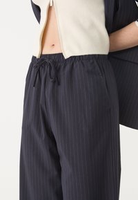 Navy-blauwe gestreepte broek met een elastische tailleband en trekkoord. Bevat zijzakken en heeft een relaxte pasvorm, gemaakt van lichte stof.